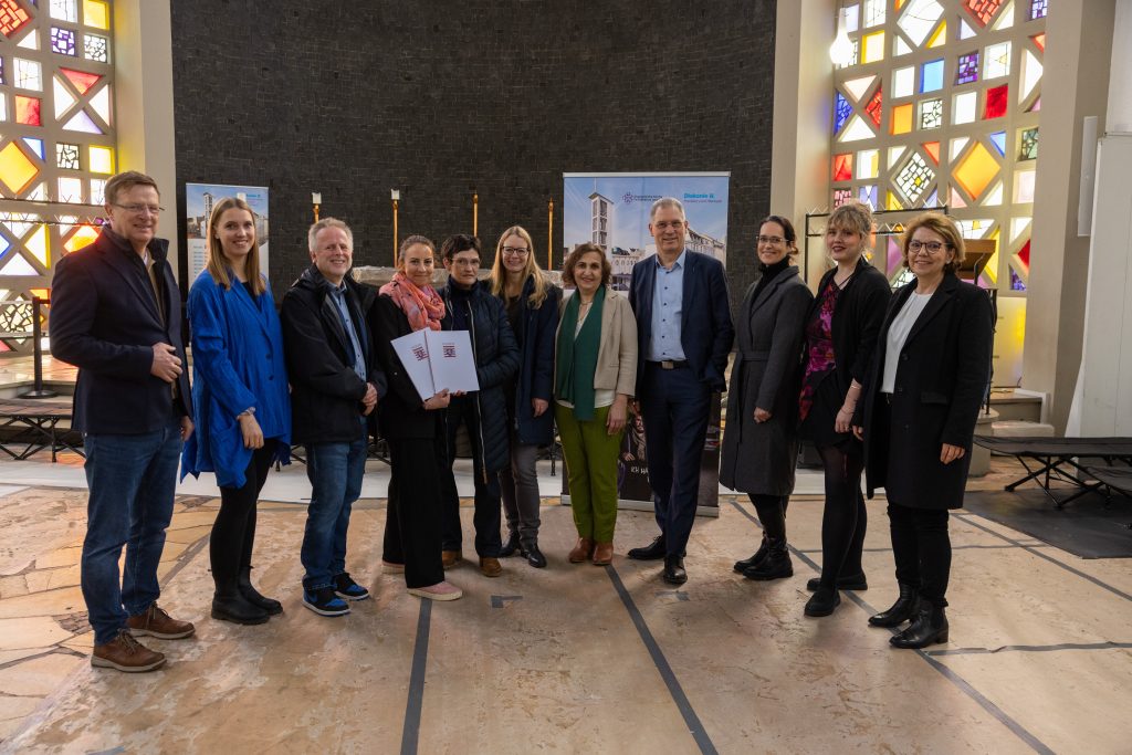 Vertreter des Evangelischen Regionalverbands Frankfurt und Offenbach stehen in der Weißfrauen-Diakoniekirche mit den Förderbescheiden. 